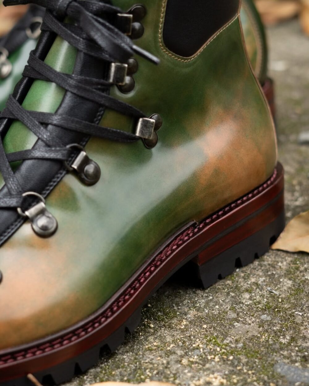A close-up of a hiking boot featuring a gradient of green and brown leather with black laces and metal eyelets.