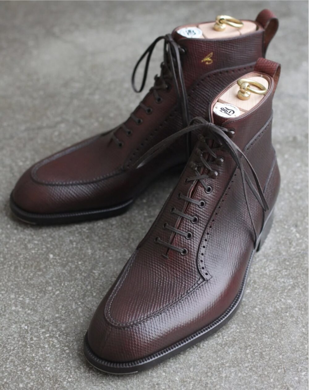 Brown leather ankle boots with a textured finish and black laces.