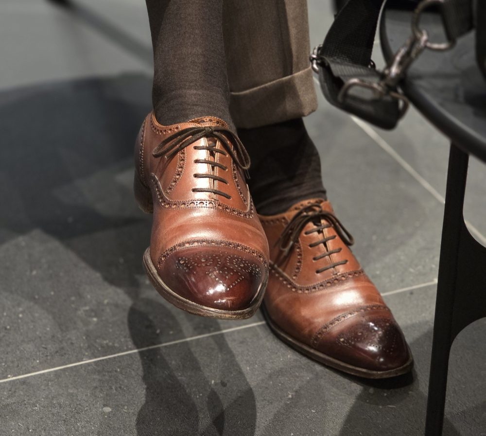 A pair of brown leather dress shoes with a glossy toe and intricate detailing on the sides.