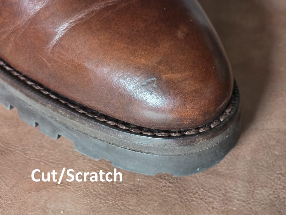 A close-up of a brown leather shoe showing a visible cut or scratch on the toe area.