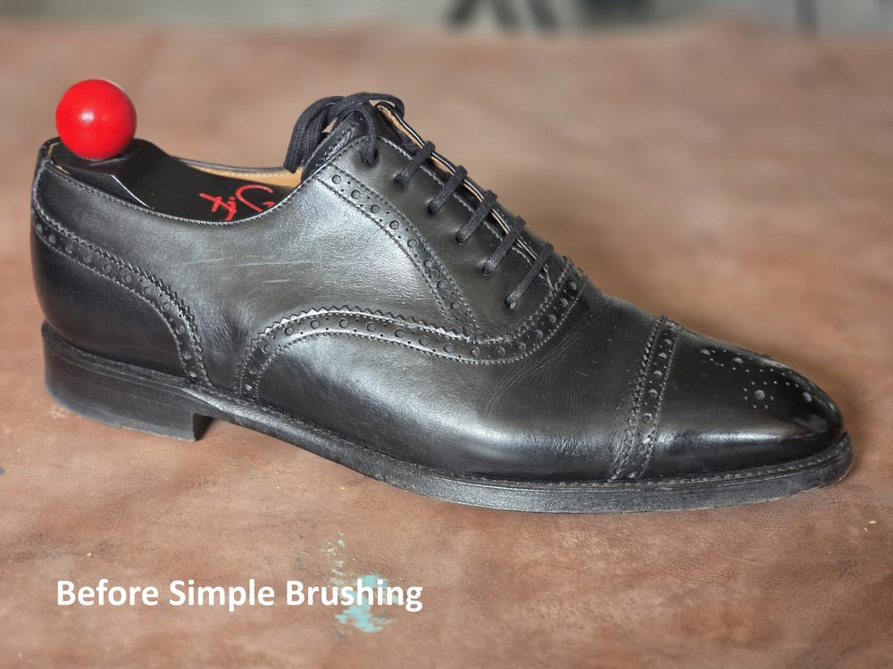 A black leather dress shoe with a red shoe tree inserted, showing visible scuffs.