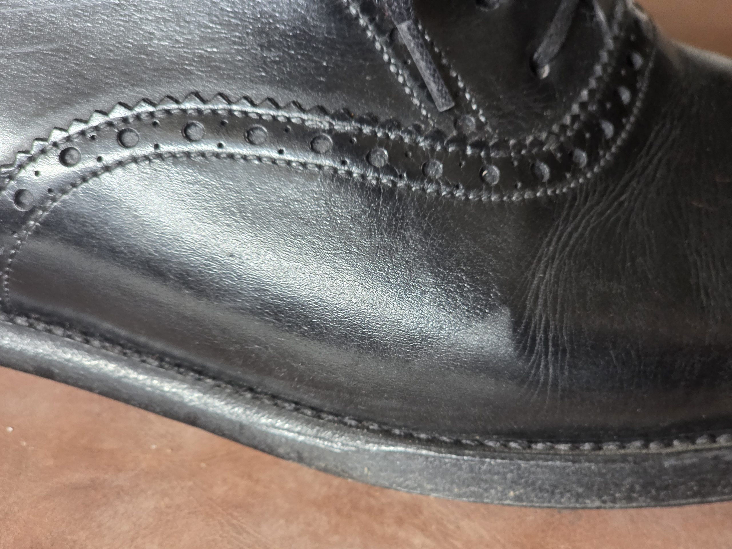 Close-up of a black leather shoe showing visible scuffs on the toe area.