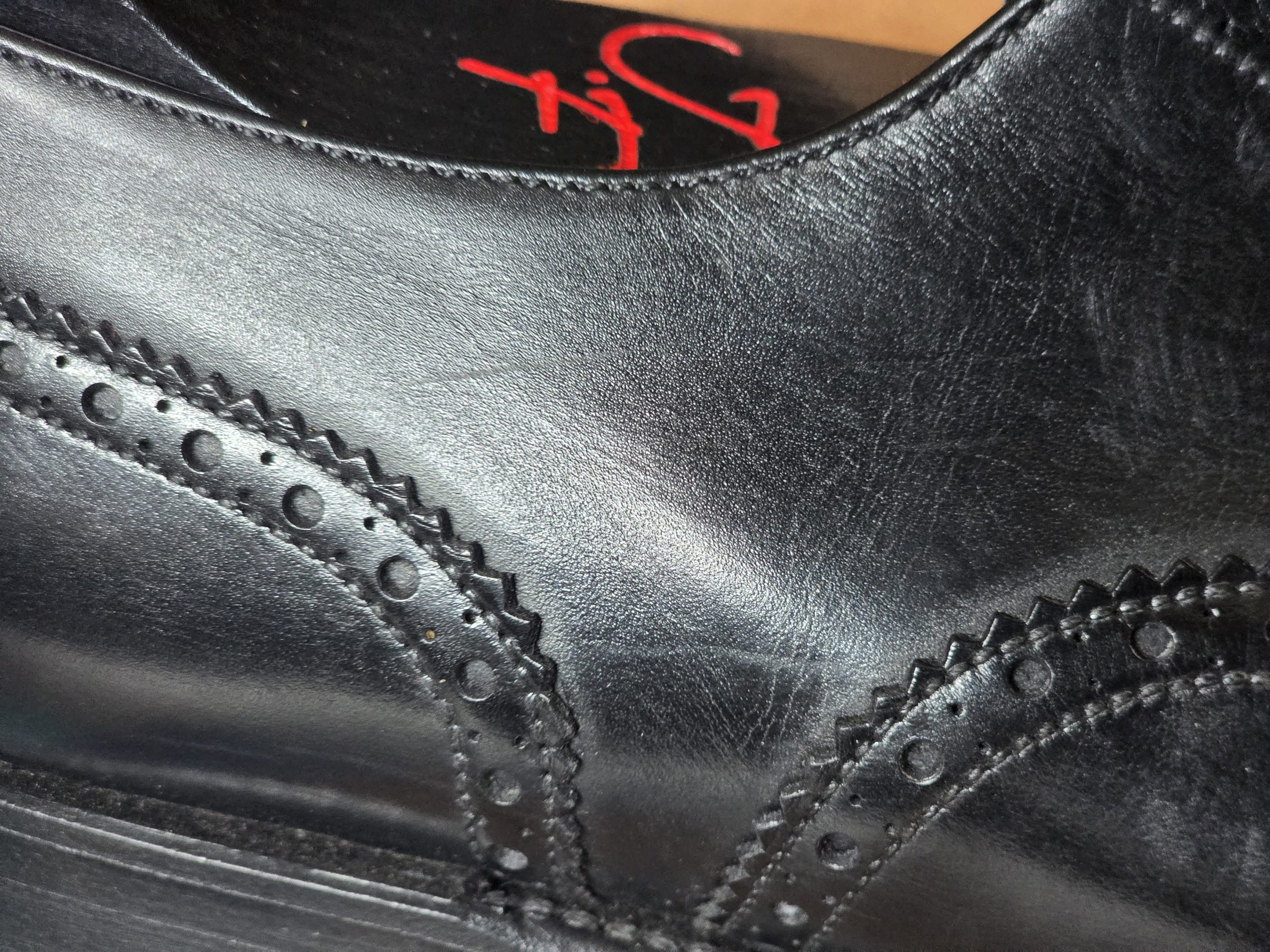Close-up of a black leather shoe showing scuffs and decorative stitching.