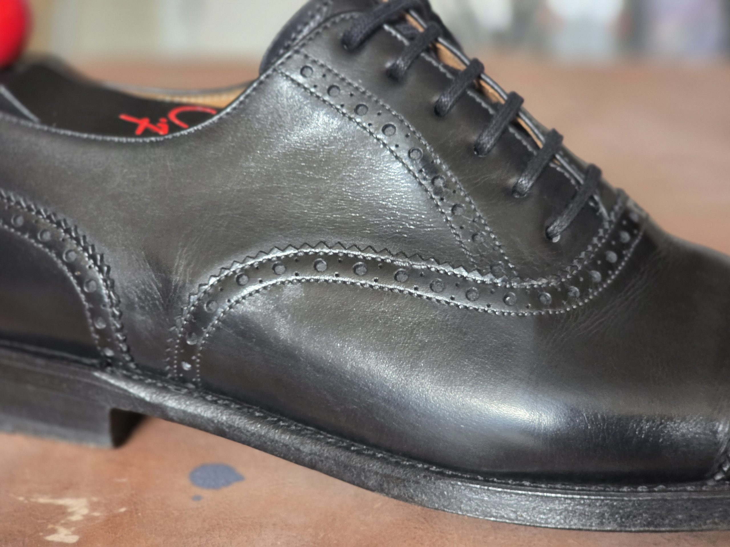 Close-up of a black leather dress shoe featuring brogue detailing and laces.