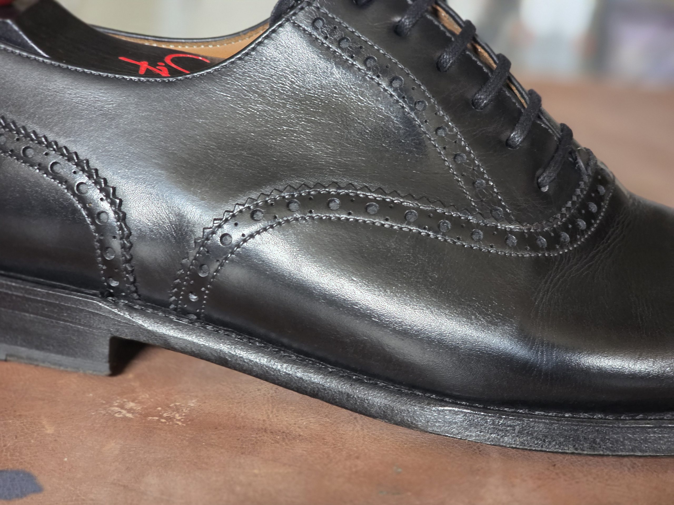 A close-up of a polished black leather dress shoe featuring decorative broguing and laces.