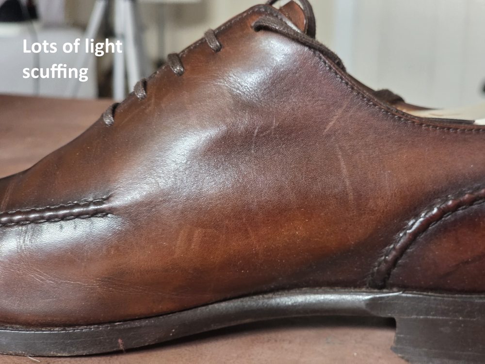 A brown leather shoe displaying lots of light scuffing on the side.