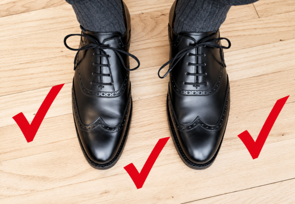 A pair of black leather dress shoes with neatly tied laces, accompanied by three red check marks.