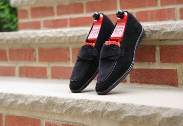 Black suede shoes with a decorative strap and red shoe trees.