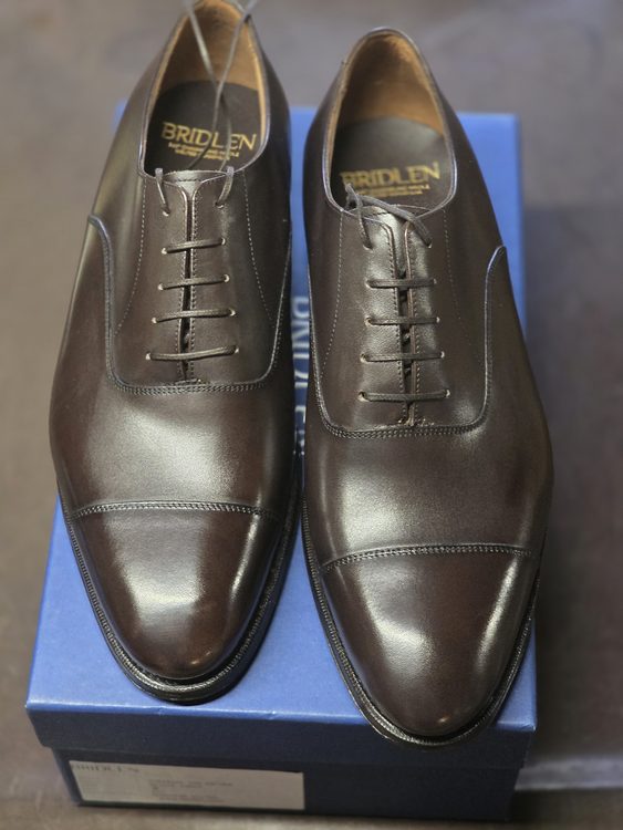 A pair of polished brown leather Oxford shoes with a lace-up design, placed on a blue box.