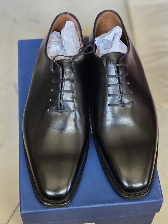 A pair of shiny black dress shoes with laces, resting on a blue box.