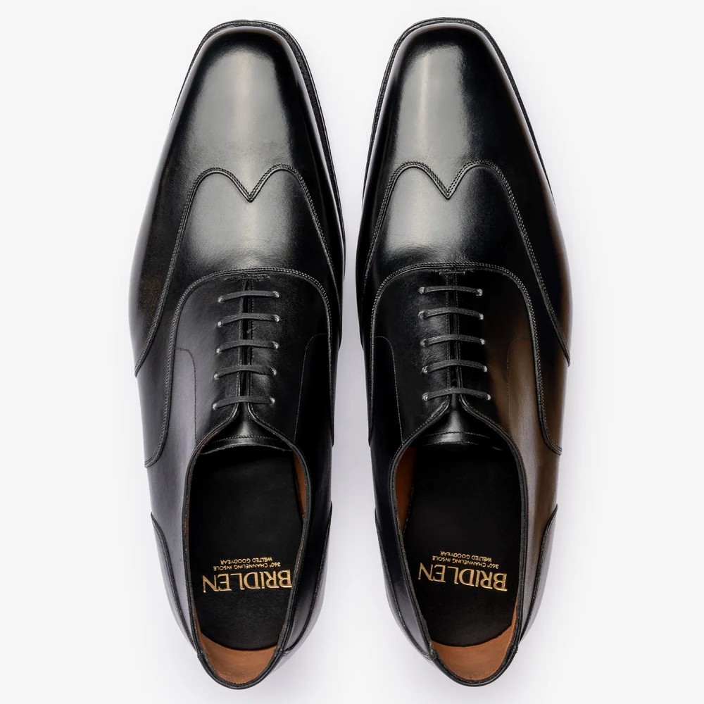 A pair of black leather dress shoes with a pointed toe and decorative stitching.