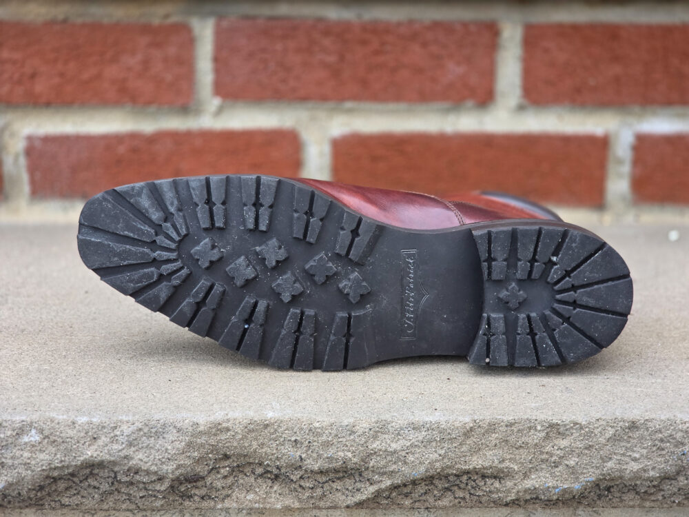 The image shows the black rubber sole of a brown leather boot with a rugged tread pattern.
