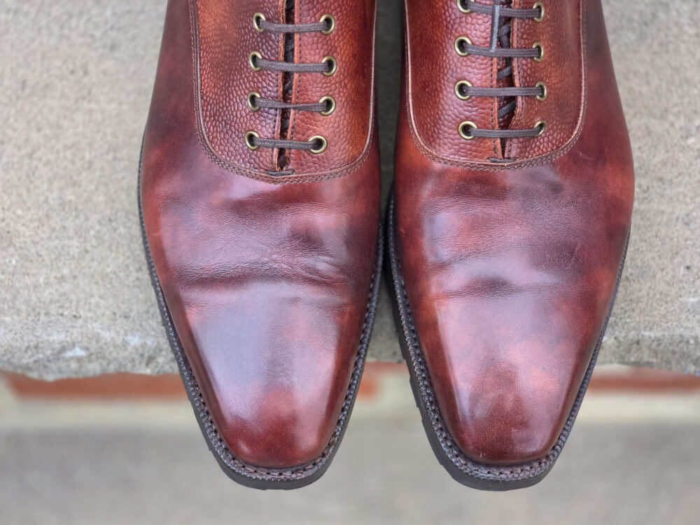 A pair of polished brown leather dress shoes with a pointed toe and laces.