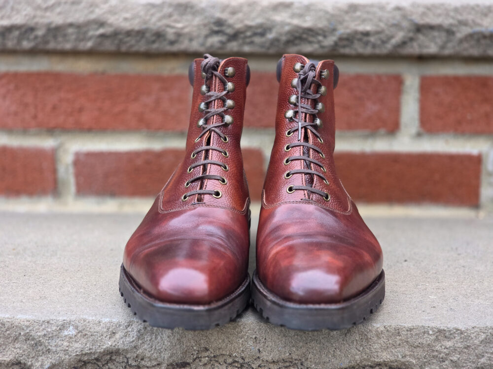 A pair of polished brown leather boots with laces and metal eyelets.