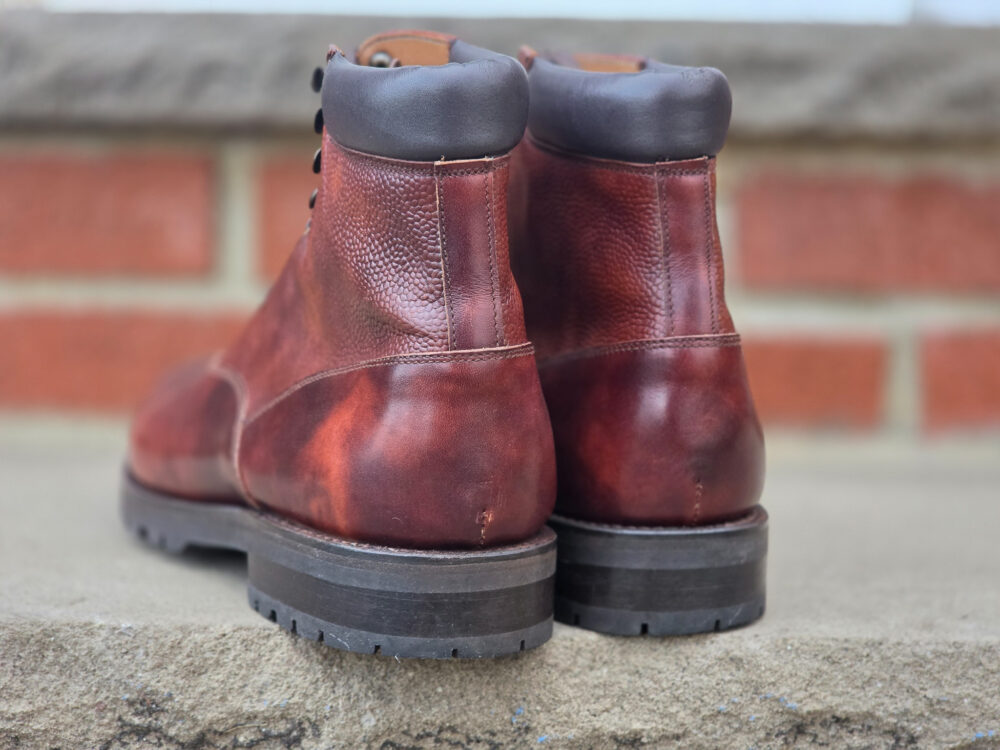 A pair of brown leather boots with a textured finish and a black padded collar, viewed from the back.