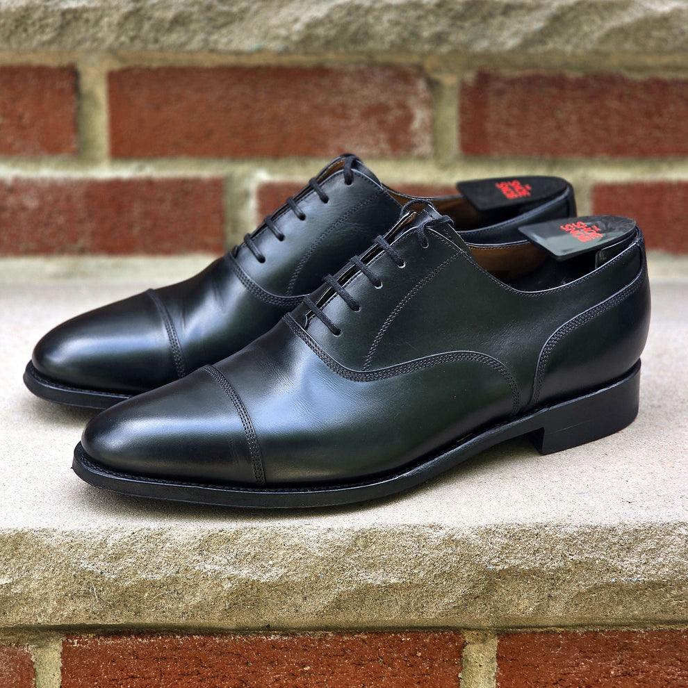 A pair of black leather dress shoes with a cap toe and lace-up design.