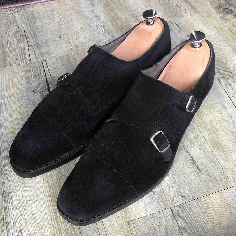 Two black suede dress shoes with silver buckles.