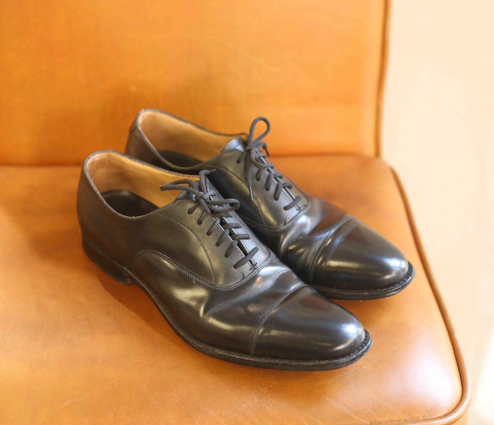 A pair of black leather dress shoes with laces and a cap toe design.