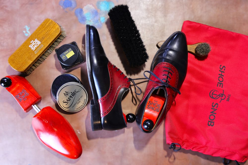 A pair of black and red dress shoes is surrounded by shoe care products, including brushes and polish, featured in a shoe care guide.