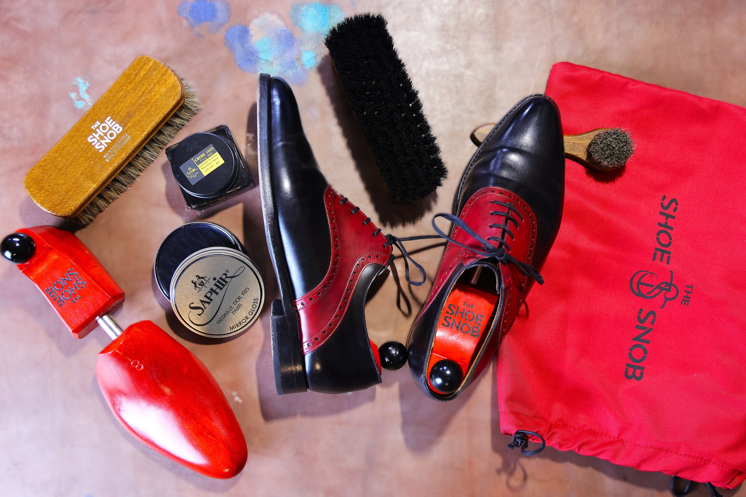 A pair of black and red dress shoes is surrounded by shoe care products, including brushes and polish, featured in a shoe care guide.
