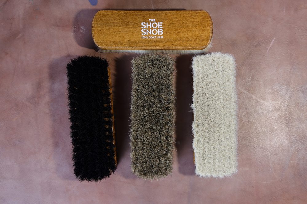 Three shoe brushes made of goat hair in black, brown, and white, labeled "The Shoe Snob," featured in a shoe care guide.