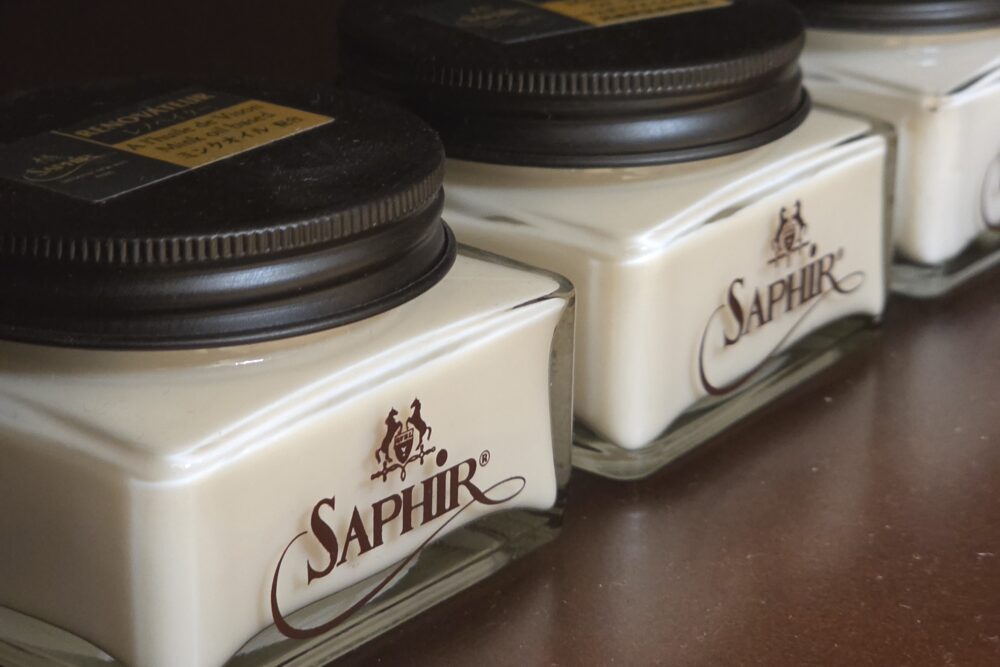 Three jars of cream labeled "Saphir," featuring a white product and dark lids, are displayed as part of a shoe care guide.