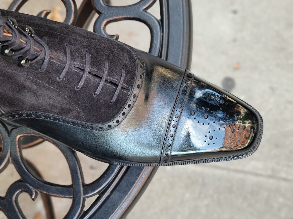 A close-up of a polished black leather shoe with suede accents, highlighting common shoe shine don'ts.