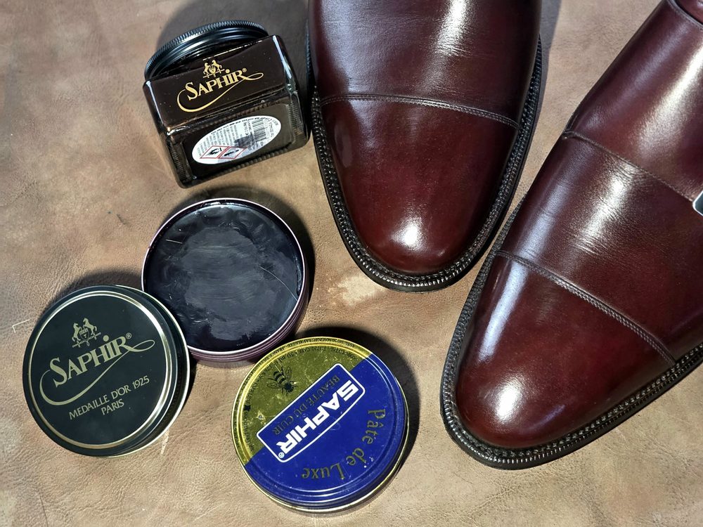 A pair of polished burgundy shoes is surrounded by various Saphir shoe care products, highlighting common shoe shine don'ts.