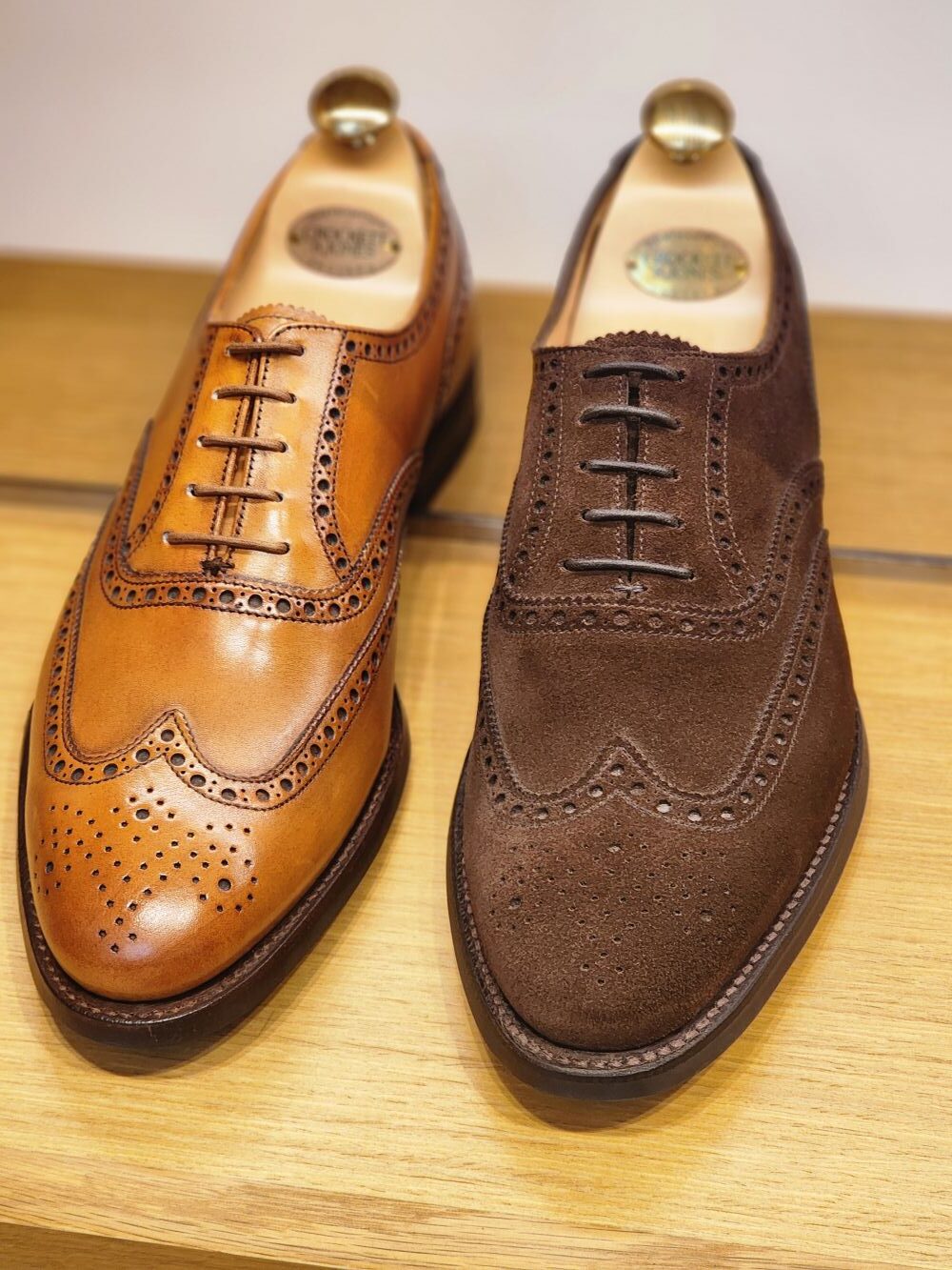 A pair of dress shoes, one in tan leather and the other in dark brown suede, showcasing detailed brogue patterns, featured in "Shoe Industry Secrets."