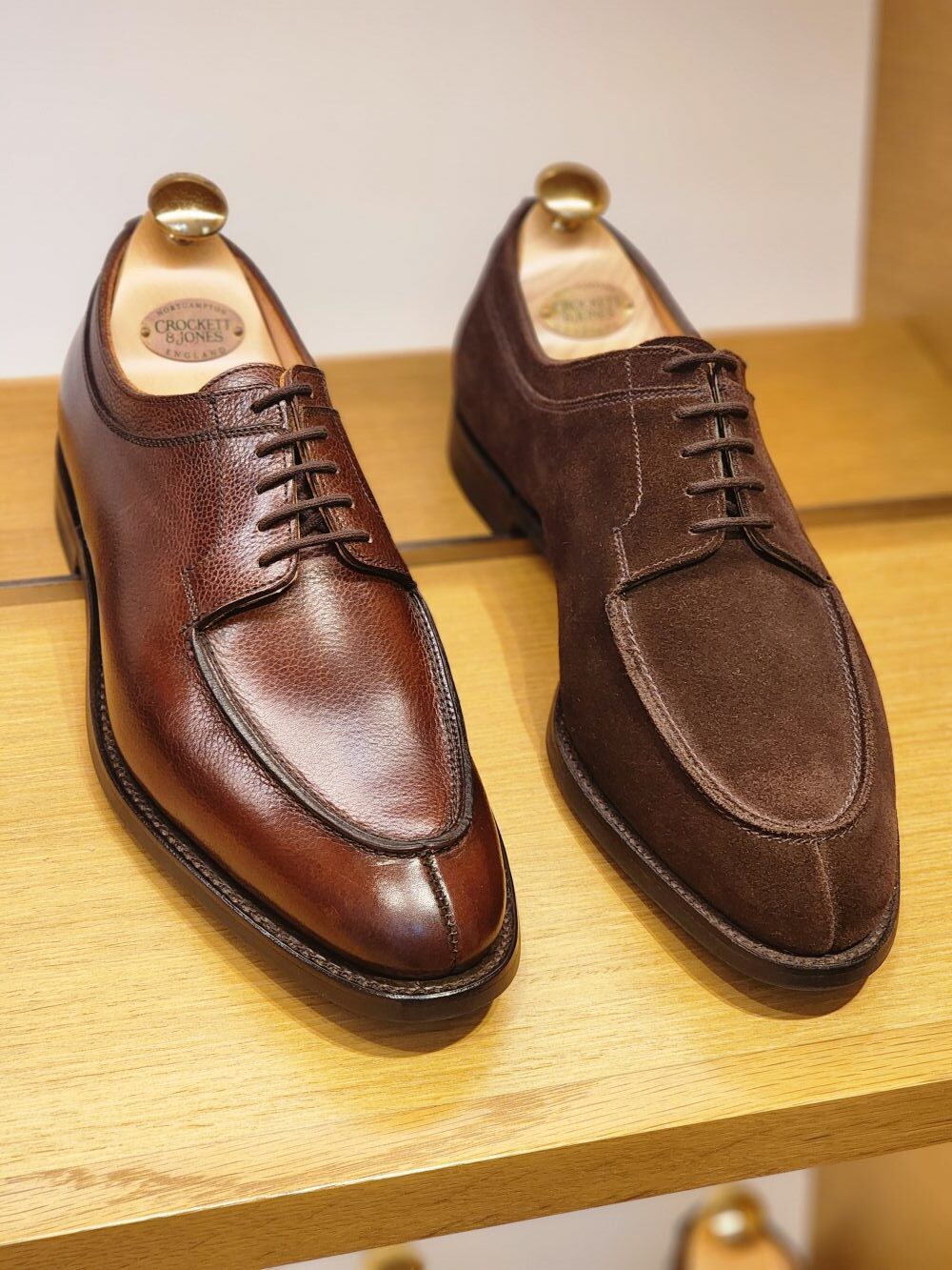 A pair of shoes featuring a polished brown leather shoe on the left and a dark brown suede shoe on the right, highlighting shoe craftsmanship in the shoe industry secrets.