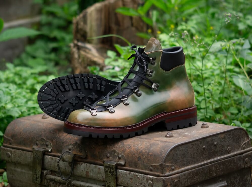 A pair of handmade leather hiking boots in green and brown, featuring black laces and a rugged sole, illustrating Shoe Industry Lies.