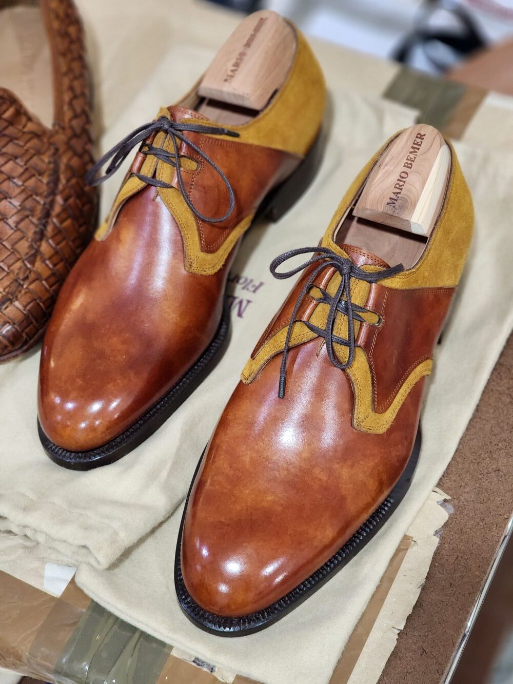 A pair of polished brown leather shoes with yellow suede accents and dark laces.