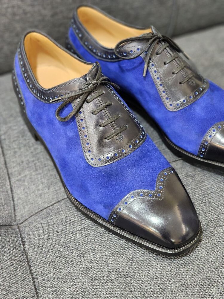 A pair of blue suede dress shoes with black leather accents and decorative perforations.