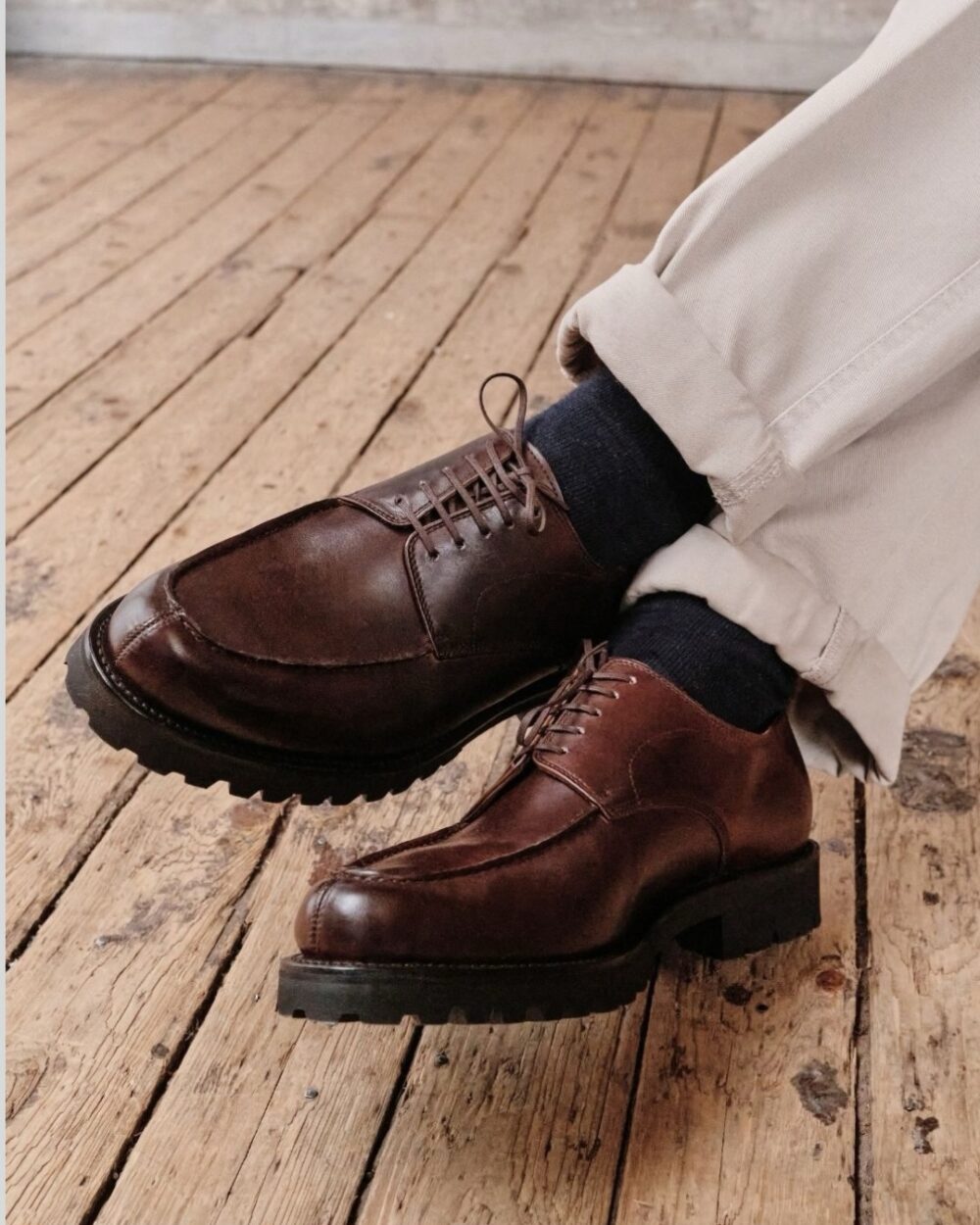 Brown leather dress shoes with a rugged sole, worn with light-colored pants and dark socks.