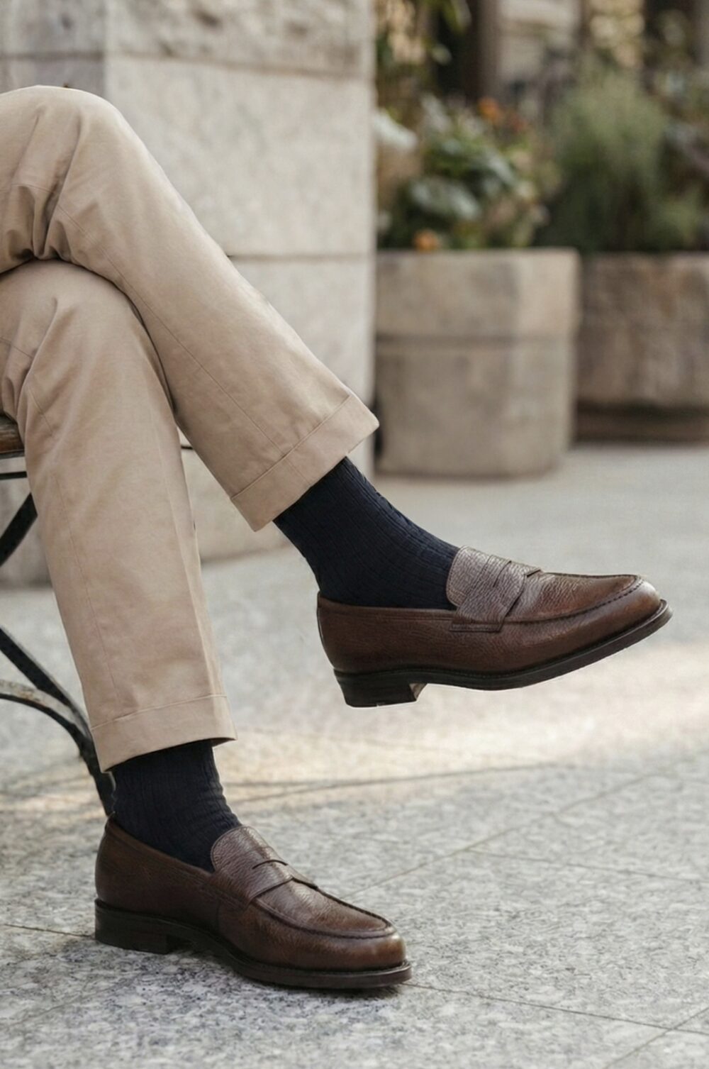 Brown leather loafers with a textured finish, paired with navy ribbed socks and khaki pants.