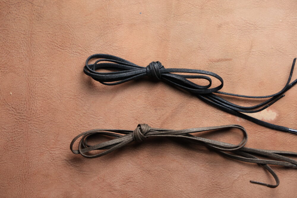 Two tied shoelaces, one black and one brown, resting on a light brown surface.