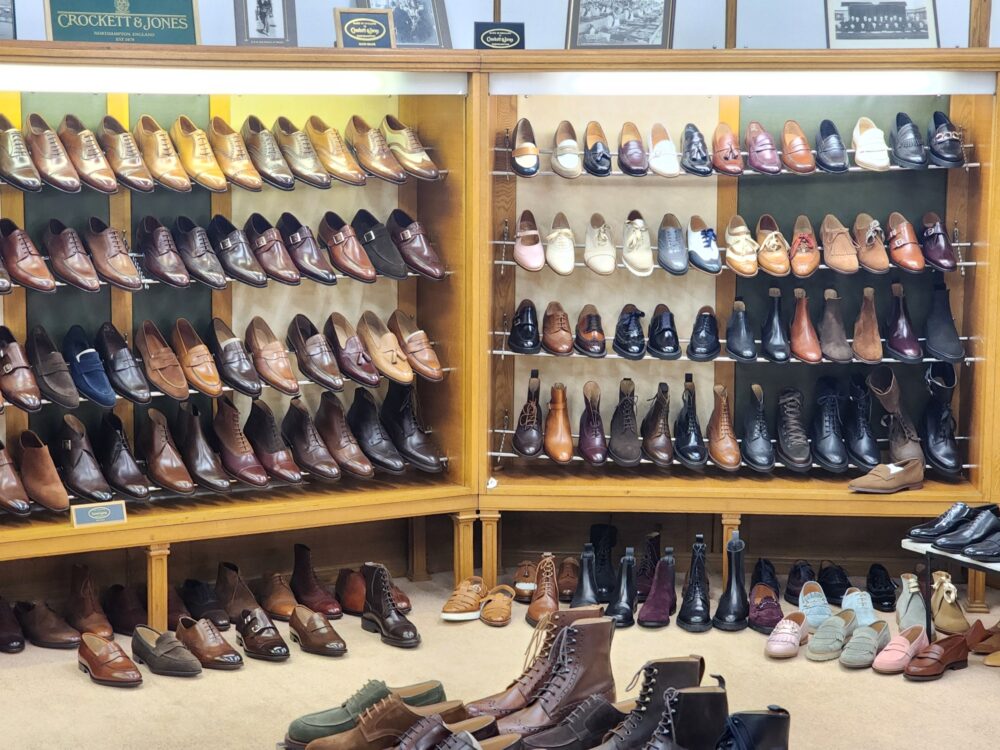 A display of various styles of leather shoes in shades of brown, black, and tan arranged on wooden shelves.