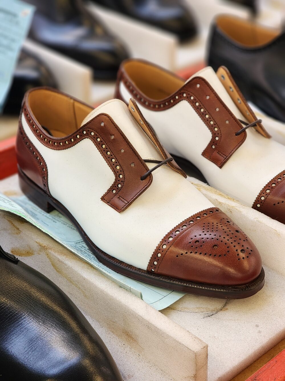 A pair of white and brown leather dress shoes with decorative perforations and laces.