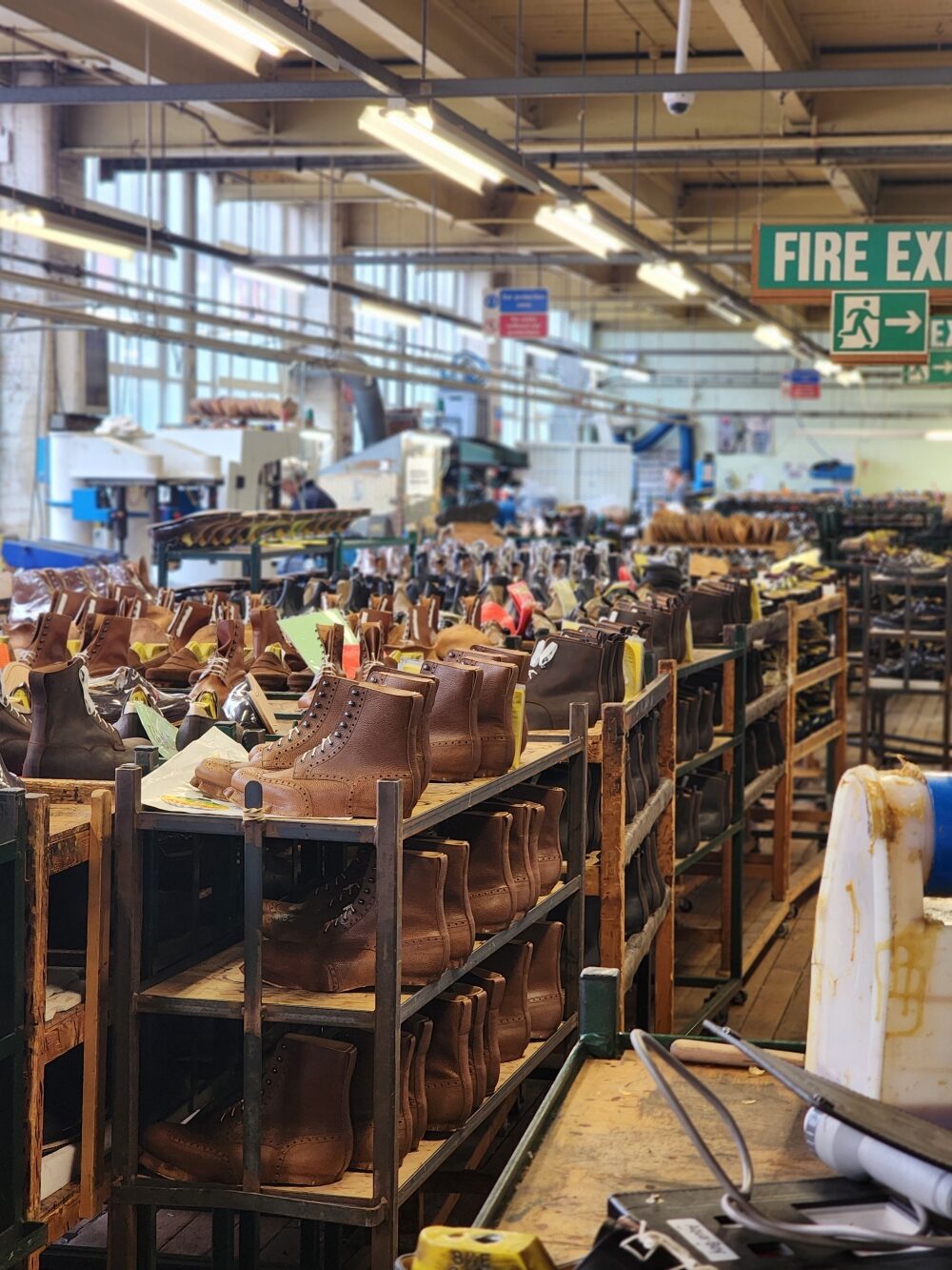 A row of brown leather boots on wooden shelves in a factory.
