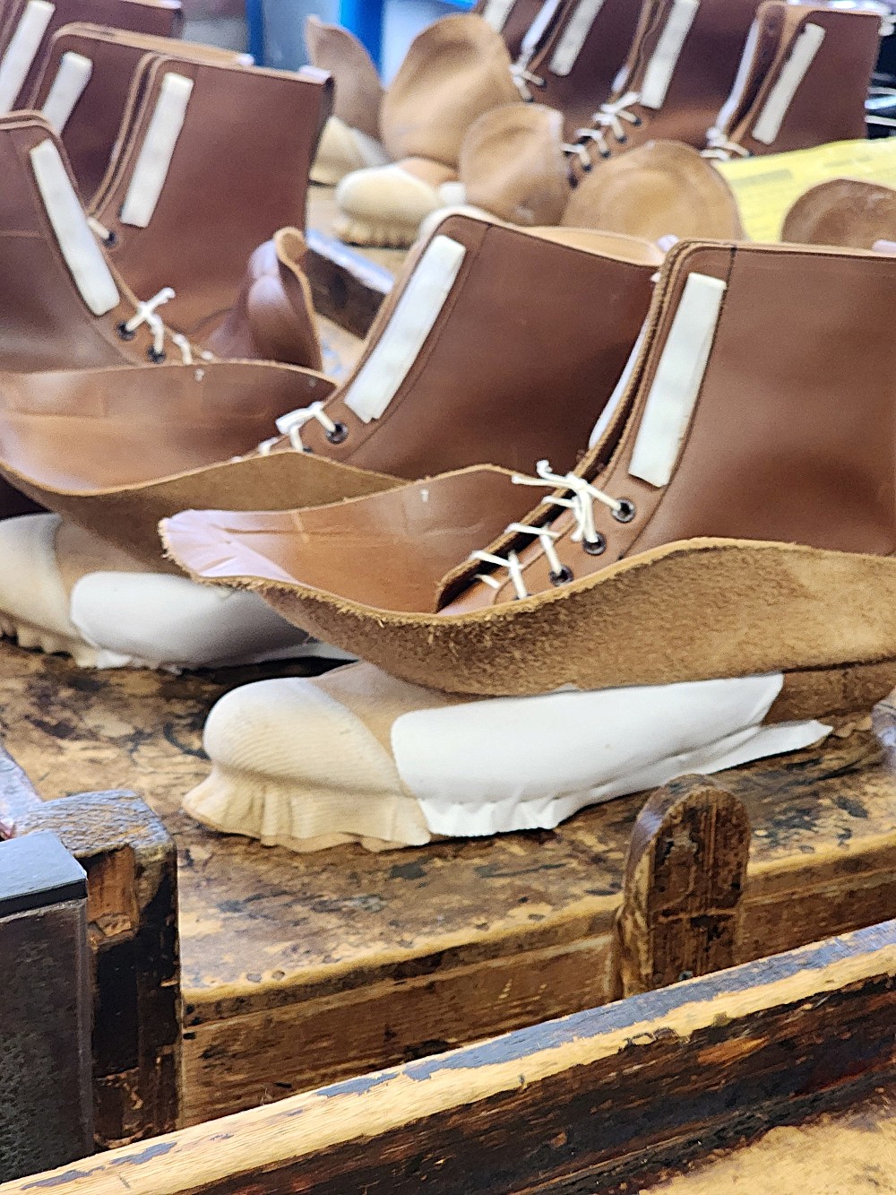 A pair of brown leather boots with white accents, displayed on a wooden surface, showcasing their unique design.