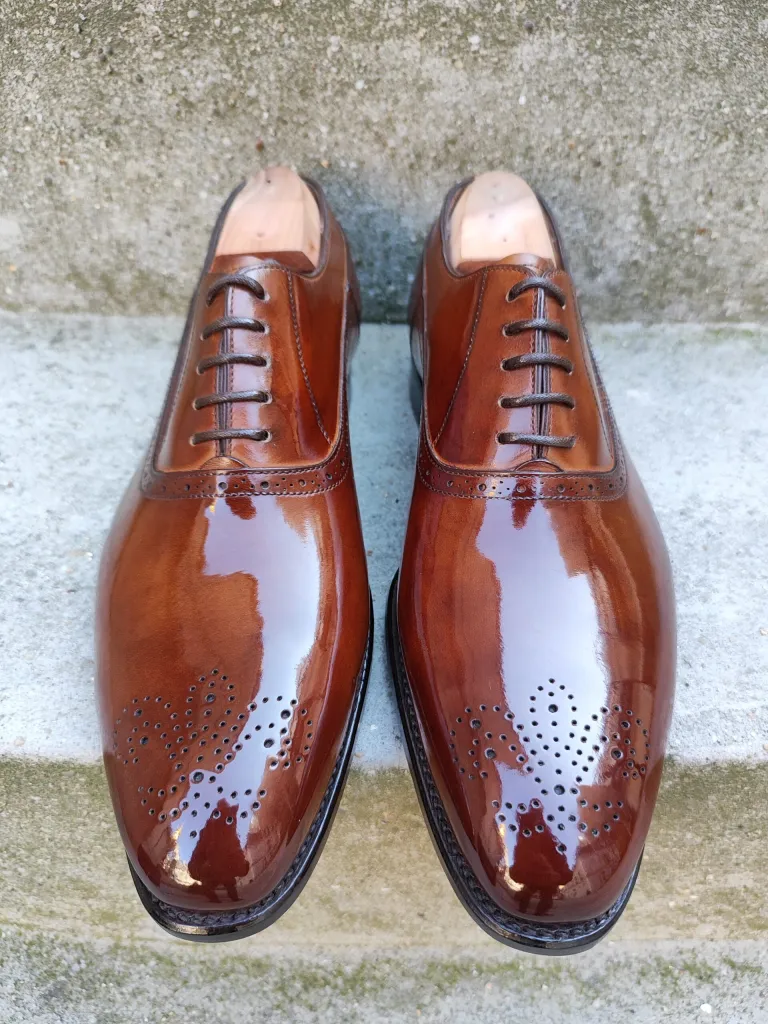 A pair of polished brown leather dress shoes with decorative perforations.