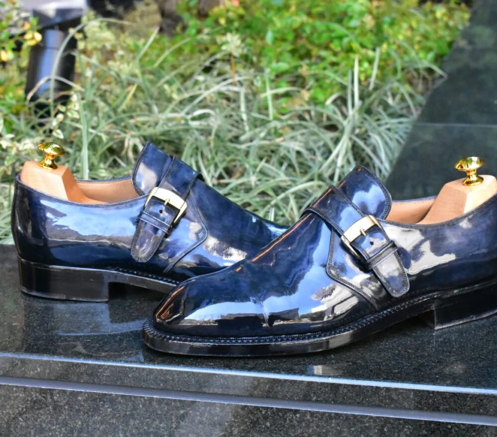 A pair of polished navy blue leather shoes with a decorative buckle and shoe trees inside.