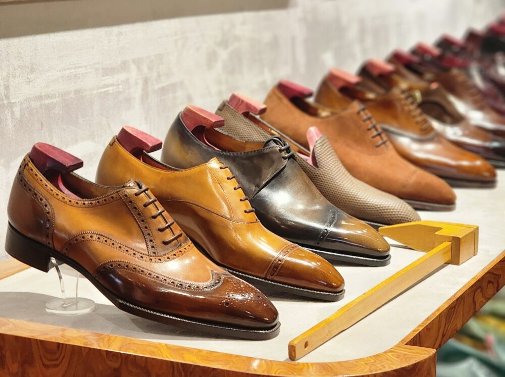 A variety of polished leather dress shoes in shades of brown and black, displayed on a wooden shelf.