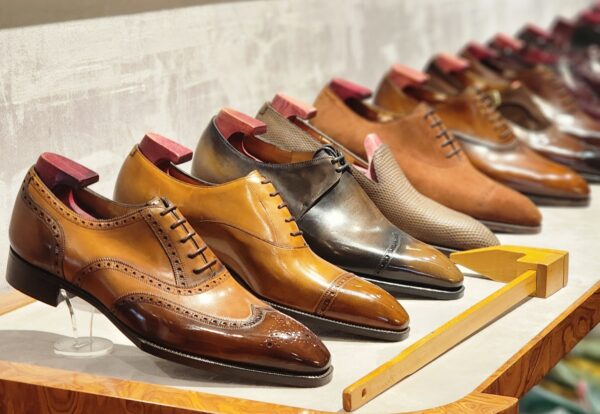A variety of polished leather dress shoes in shades of brown and black, displayed on a wooden shelf.