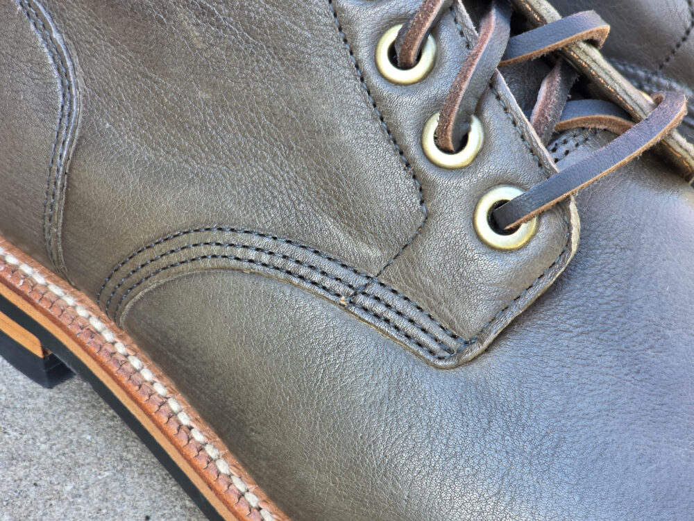Close-up of a dark green leather boot with brass eyelets and brown laces.