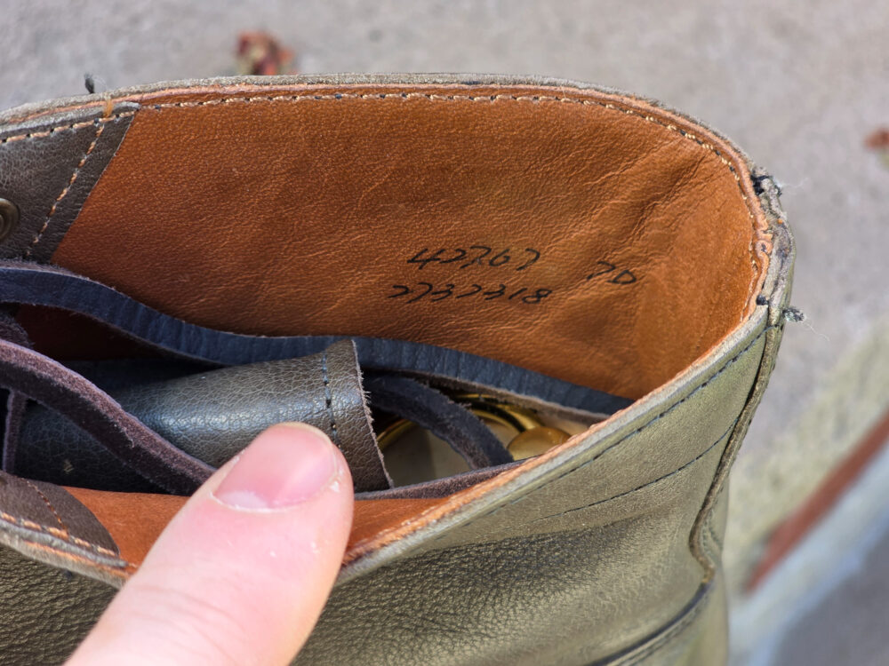 A close-up view of the interior of a brown leather boot, showing a finger pointing to the size and model number written inside.