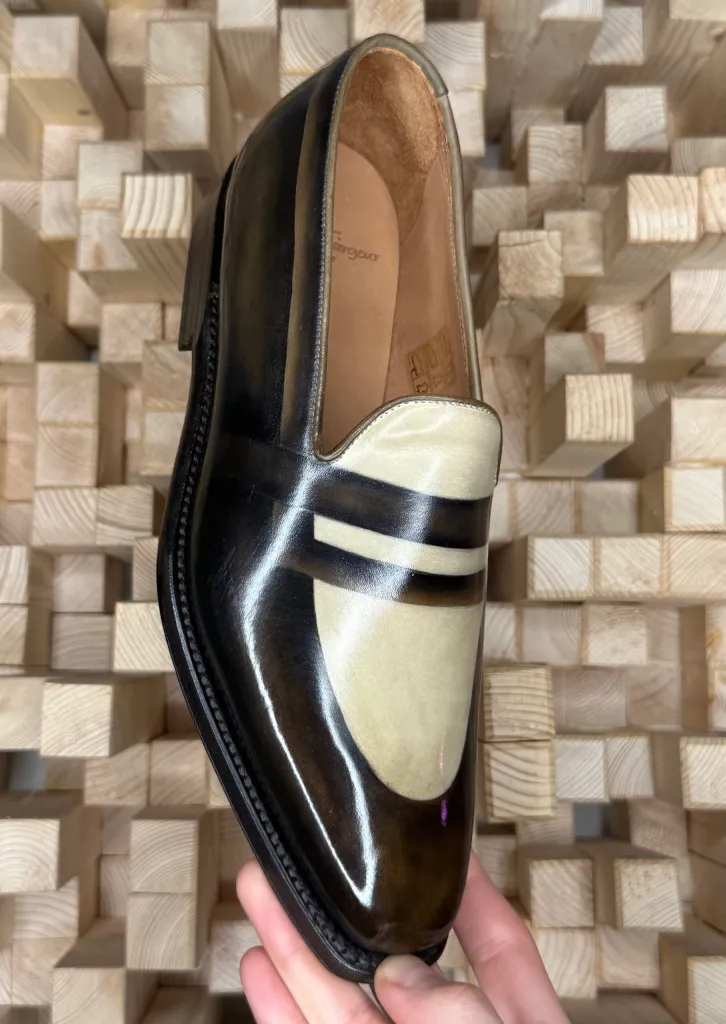 A polished brown leather shoe with a cream-colored toe cap and striped detailing.