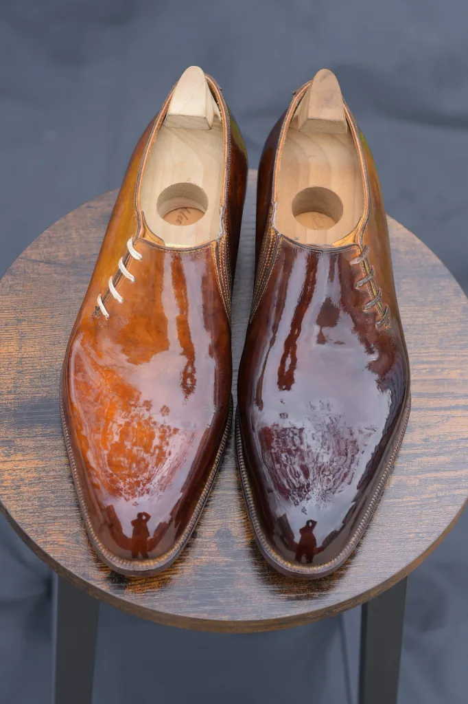 A pair of polished leather dress shoes in shades of brown, displayed on a wooden table.