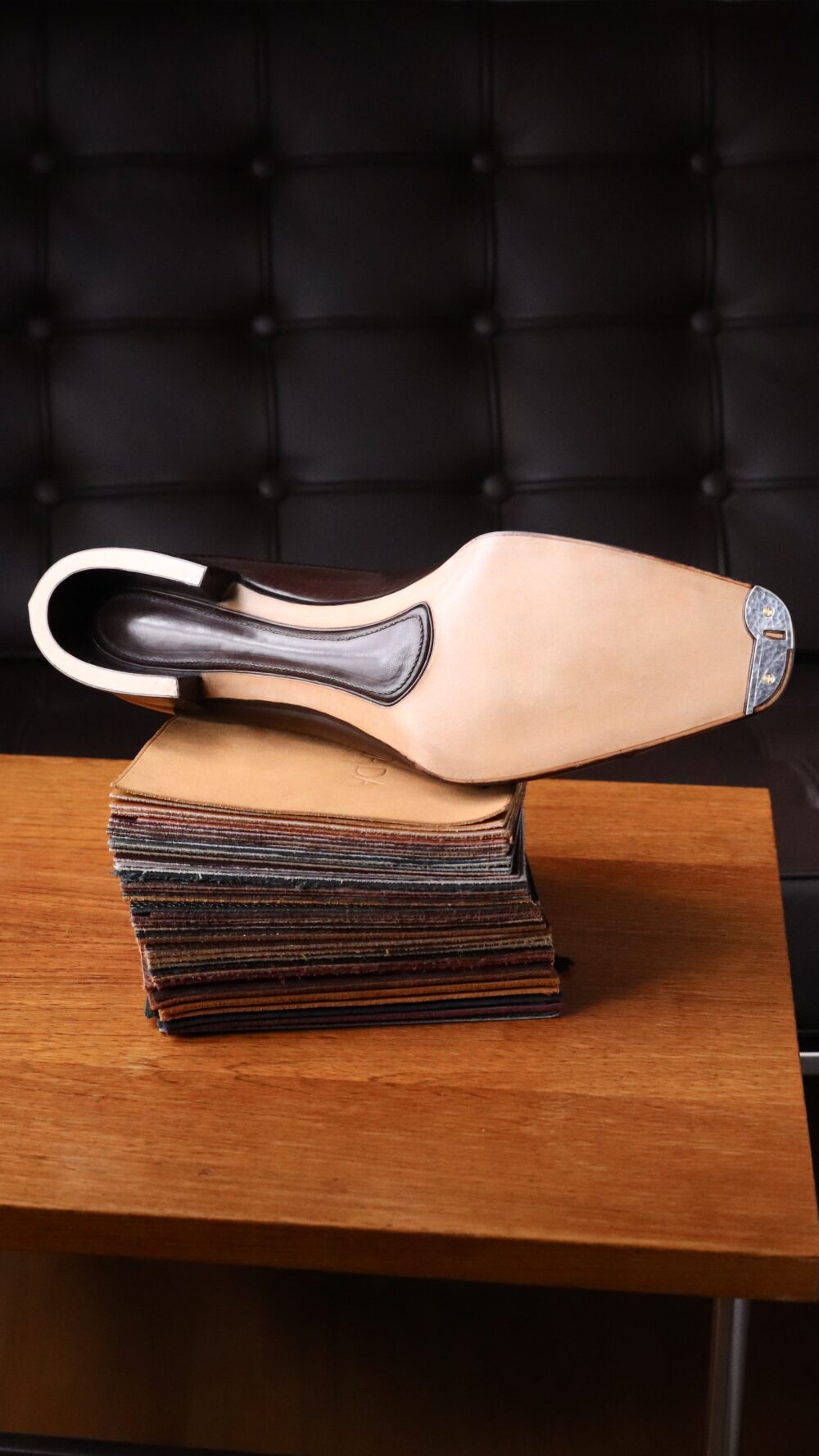 A high-heeled shoe with a light-colored sole and a dark upper rests on a stack of leather swatches.