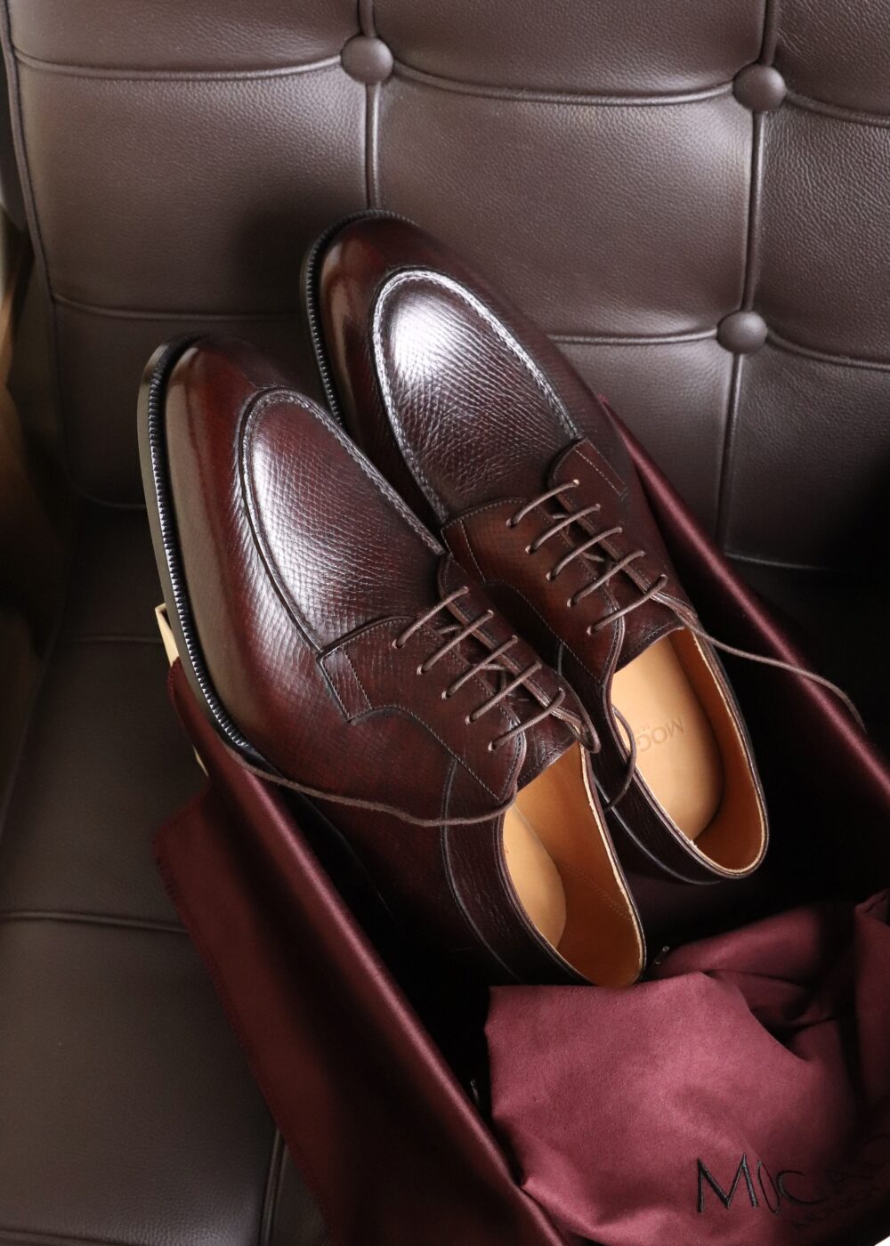 A pair of dark burgundy leather dress shoes with a textured surface and brown laces.